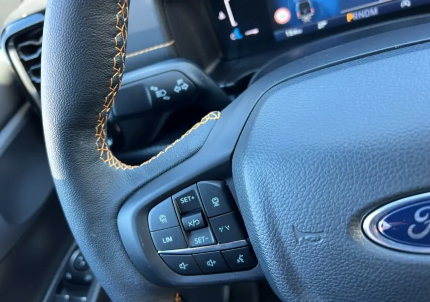 Gros plan sur le volant cuir noir avec surpiqûres marron du Ford Ranger gris carbone, boutons multifonctions visibles.