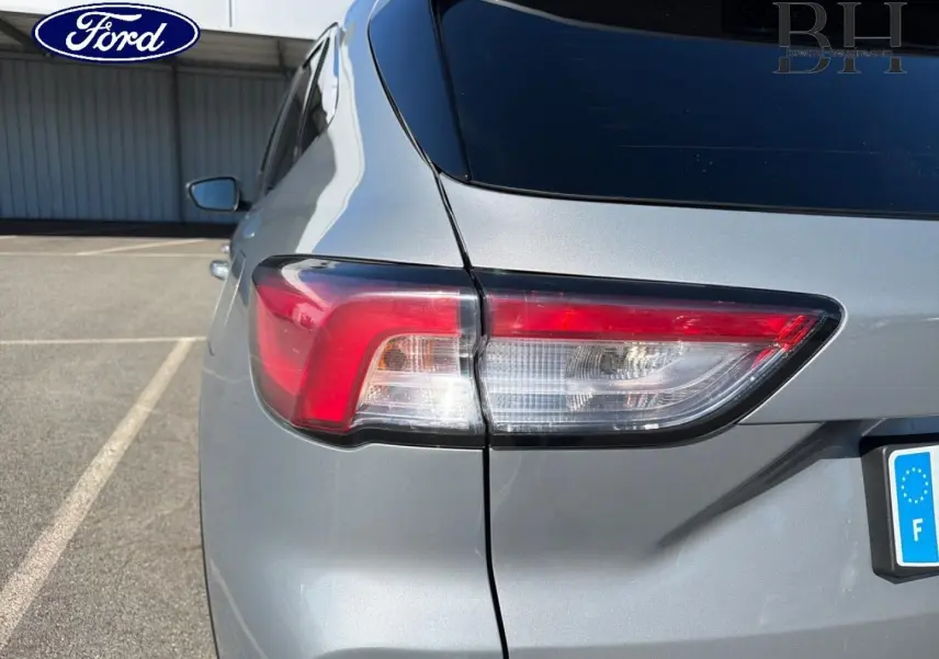 Gros plan sur le feu arrière gauche d’un Ford Kuga gris Solar métallisé, avec vitre arrière surteintée visible.