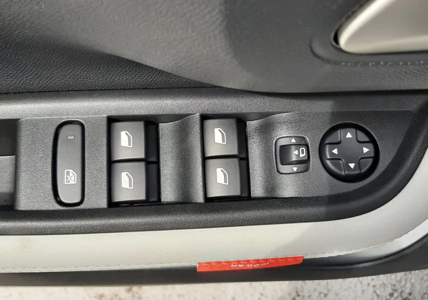 Gros plan sur les commandes de lève-vitres et réglage des rétroviseurs côté conducteur d'une Citroën C3 Aircross blanc banquise avec intérieur noir et blanc.