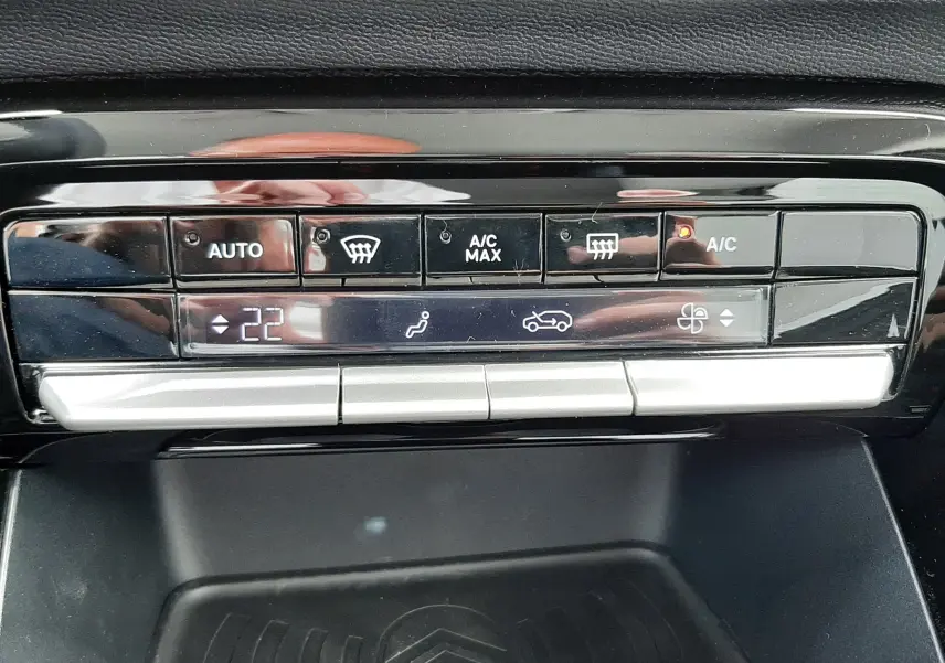 Gros plan sur la commande de climatisation digitale et le support de charge sans fil avec logo Citroën, intérieur noir.