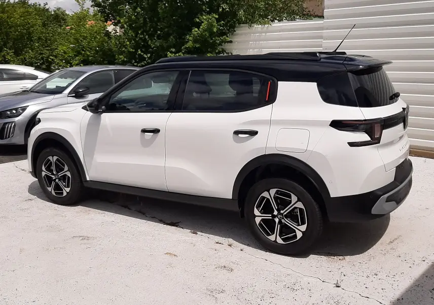 Vue 3/4 arrière côté droit d'un Citroën C3 Aircross blanc banquise avec toit noir et jantes noires et argentées.