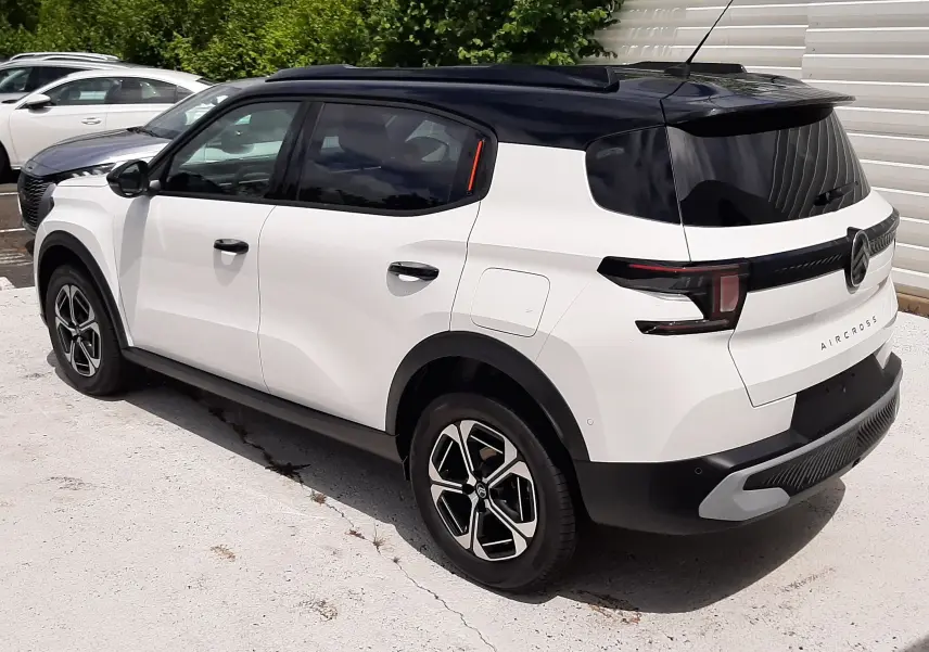 Vue 3/4 arrière droite du Citroën C3 Aircross blanc banquise avec toit noir et jantes bi-ton, garé en extérieur.