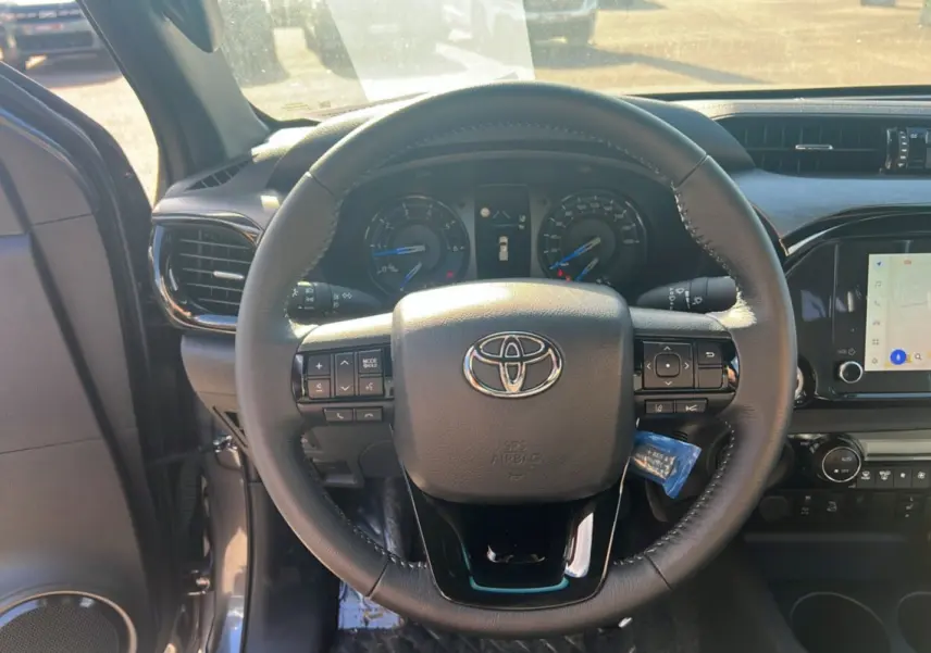 Vue intérieure centrée sur le volant du Toyota Hilux 2025 gris atlas, avec tableau de bord et écran tactile visibles.
