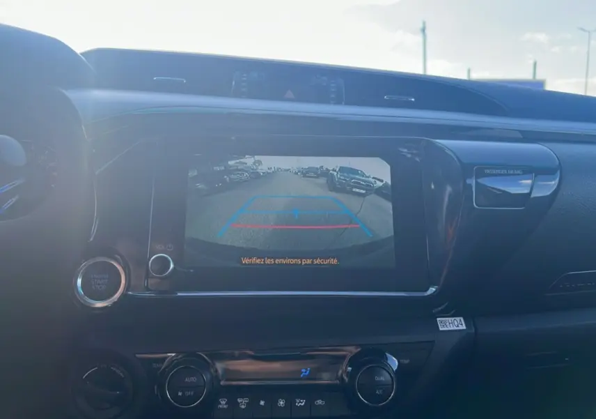 Vue intérieure du tableau de bord du Toyota Hilux 2025 avec écran de caméra de recul et commandes climatisation visibles.
