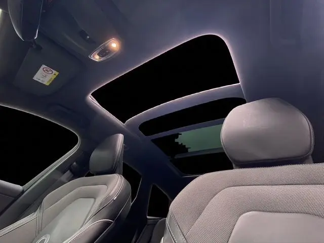 Intérieur du Volvo XC60 noir 2021, vue sur sièges avant et toit panoramique ouvert éclairé de nuit.