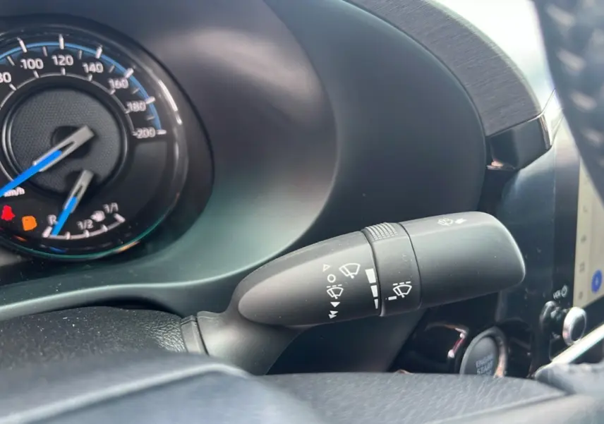 Gros plan sur le commodo d'essuie-glace et le compteur du Toyota Hilux 2025 gris atlas, intérieur moderne et fonctionnel.