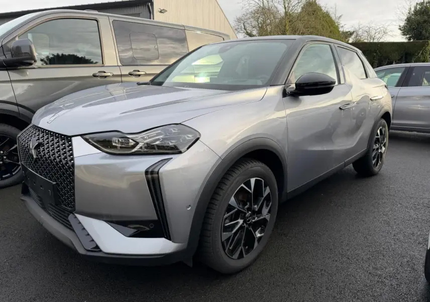 DS3 2024 gris Artense avec toit noir, vue 3/4 avant droit, calandre noire brillante et jantes alliage 18 pouces.