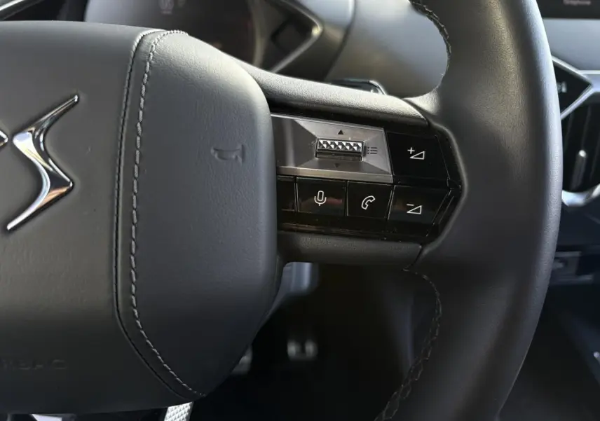 Gros plan sur le volant cuir noir du DS3 2024, avec commandes intégrées et logo DS chromé visible.