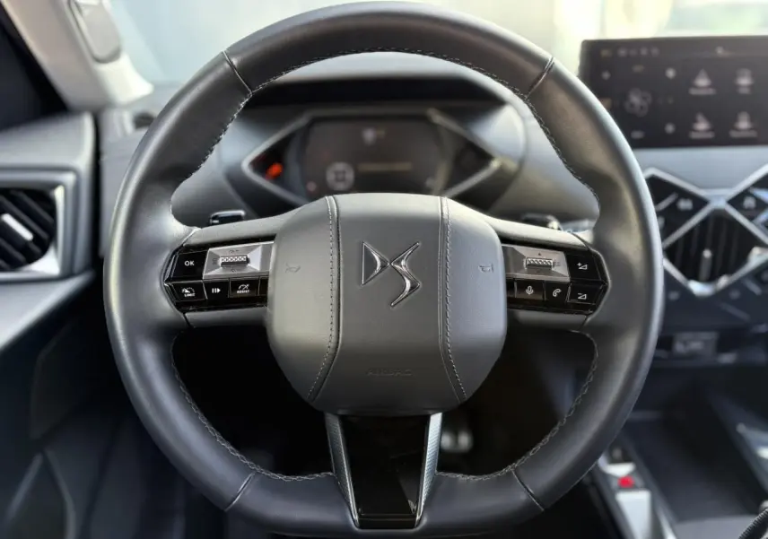 Volant cuir noir DS3 2024 avec commandes intégrées, tableau de bord numérique et écran tactile en arrière-plan.