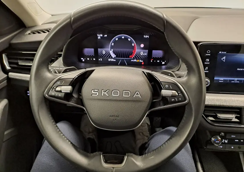 Vue intérieure centrée sur le volant noir SKODA d'un KAMIQ 2025 avec tableau de bord numérique et écran tactile.