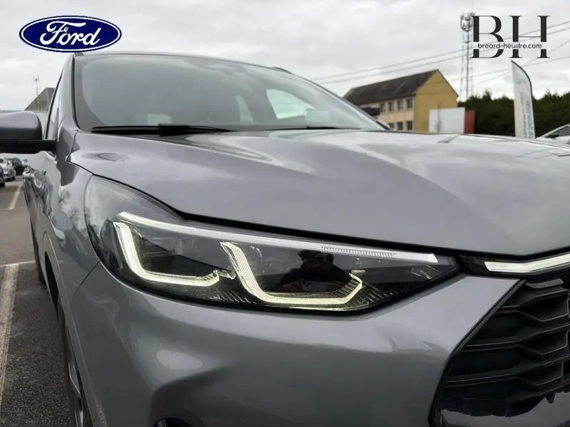 Gros plan sur le phare avant gauche du Ford Kuga 2024 gris Solar Métallisé avec calandre noire et logo Ford partiel visible.