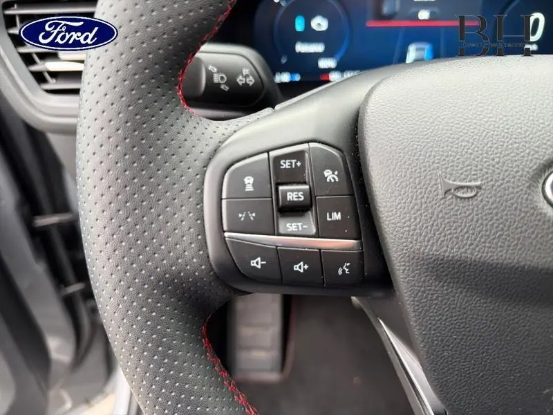 Gros plan sur le volant perforé avec surpiqûres rouges du Ford Kuga 2024, montrant les commandes multifonctions côté gauche.