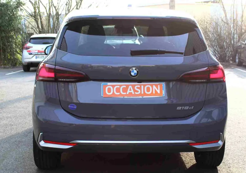 Vue arrière d'une BMW Série 2 Active Tourer gris Nardo métallisé avec feux arrière allumés et plaque "OCCASION" visible.