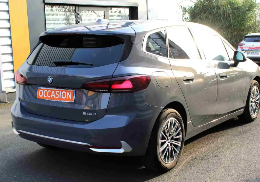 BMW Série 2 Active Tourer gris Nardo métal vue 3/4 arrière droit avec feux arrière allumés et jantes multibranches.