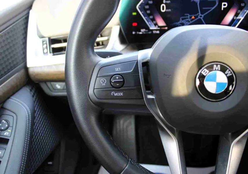 Gros plan sur le volant cuir noir et le tableau de bord digital d'une BMW Série 2 Active Tourer 218d 2023.