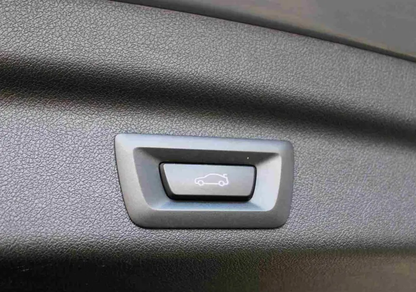 Bouton d'ouverture électrique du hayon sur panneau intérieur noir d'une BMW Série 2 Active Tourer gris Nardo.