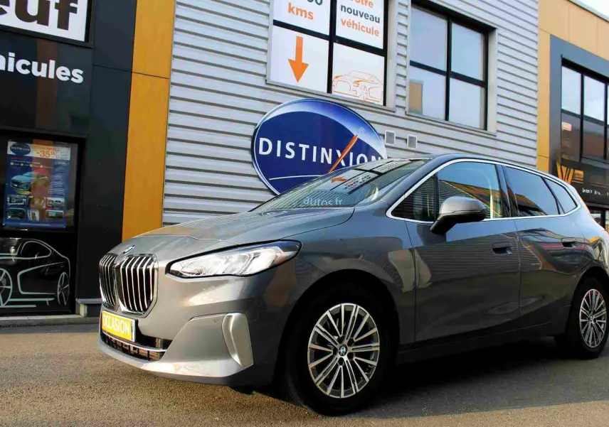 BMW Série 2 Active Tourer gris Nardo métal vue 3/4 avant droit devant un bâtiment commercial.