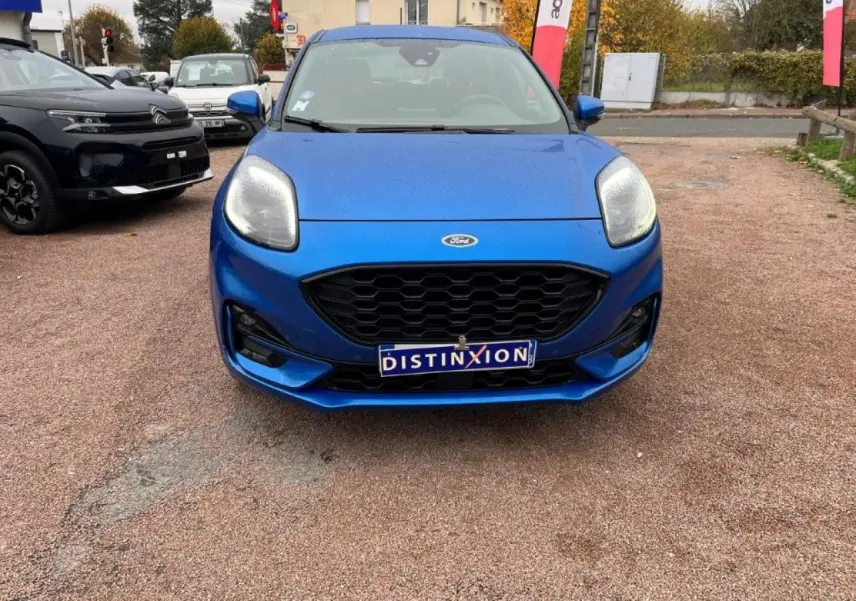Vue frontale d'une Ford Puma bleu métallisé avec calandre noire et phares LED, sur un parking extérieur.