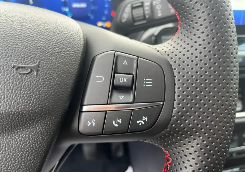 Gros plan sur les commandes multifonctions à droite du volant perforé avec surpiqûres rouges du Ford Puma bleu 2022.