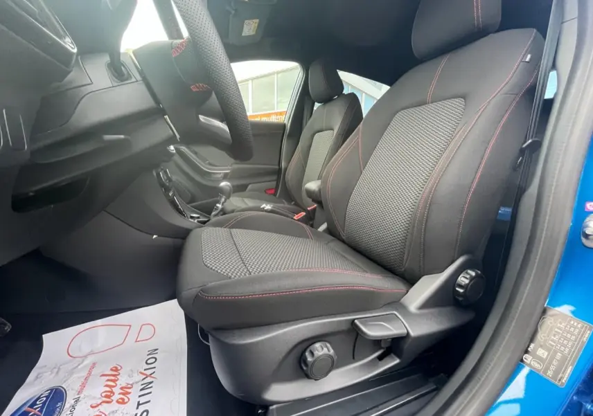 Vue intérieure côté conducteur du Ford Puma bleu 2022, sièges tissu noir avec surpiqûres rouges et volant sport.