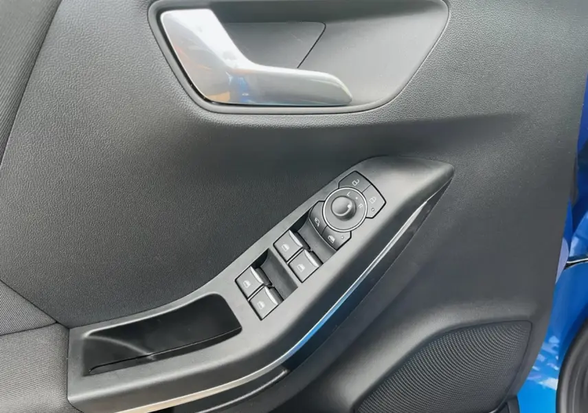 Gros plan sur la porte avant gauche du Ford Puma bleu, montrant les commandes des vitres et le haut-parleur intégré.