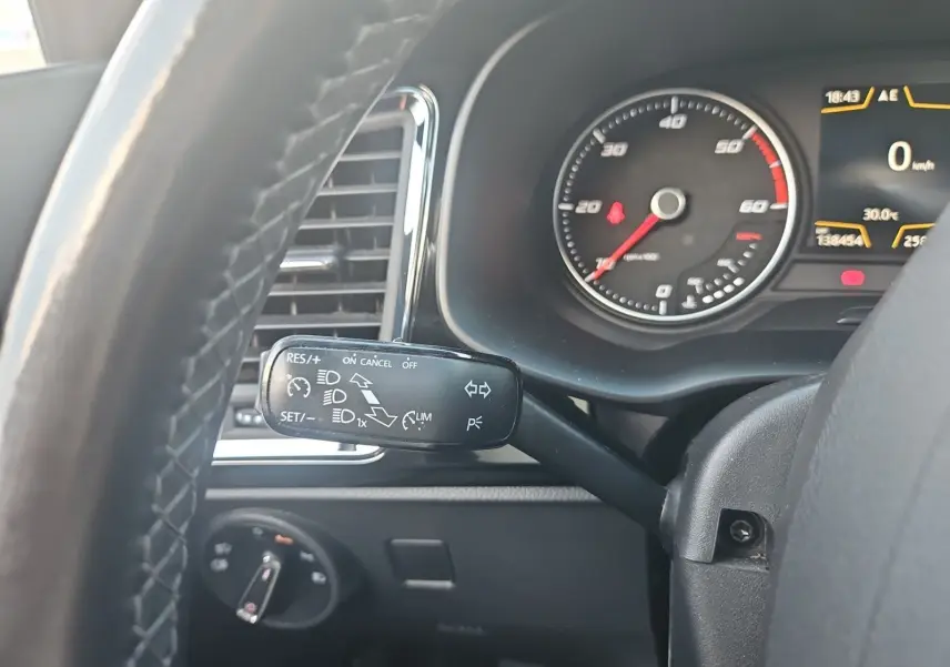 Gros plan sur le commodo gauche du volant en cuir du SEAT Ateca blanc, avec tableau de bord et compteur visible.