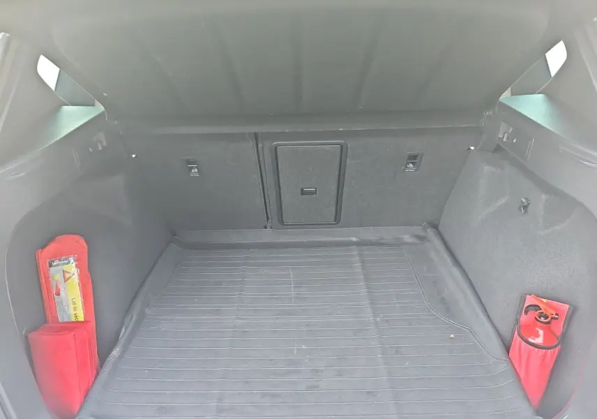 Coffre ouvert d'un SEAT Ateca blanc, vue intérieure montrant tapis de sol et équipements de sécurité rouges.