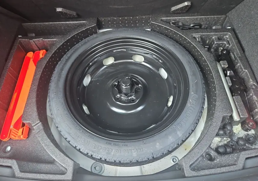 Vue plongeante sur la roue de secours galette noire et les outils de bord dans le coffre d'un SEAT Ateca blanc.