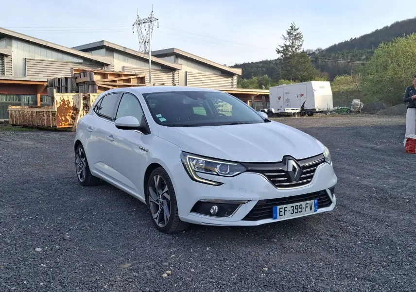 Renault Mégane blanc vue 3/4 avant droit sur sol gravillonné avec jantes alliage et calandre chromée.