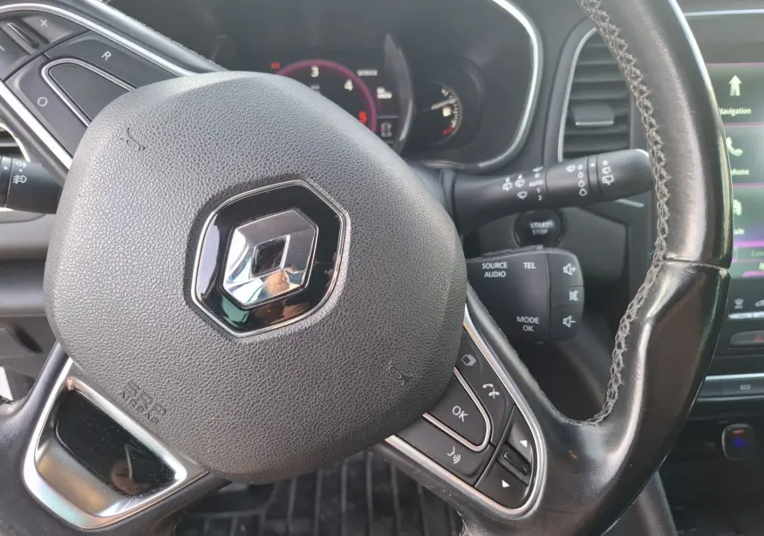 Vue rapprochée du volant noir de la Renault Mégane 1.6 DCI 130 Energy Intens avec commandes intégrées et tableau de bord en arrière-plan.