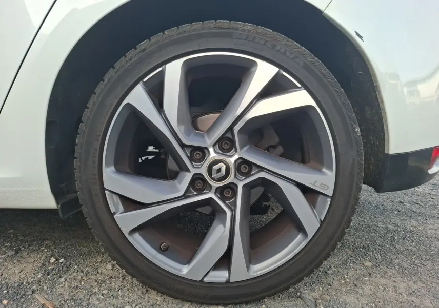 Gros plan sur la roue arrière droite d’une Renault Mégane blanche, jante alliage gris foncé GT 15 pouces.