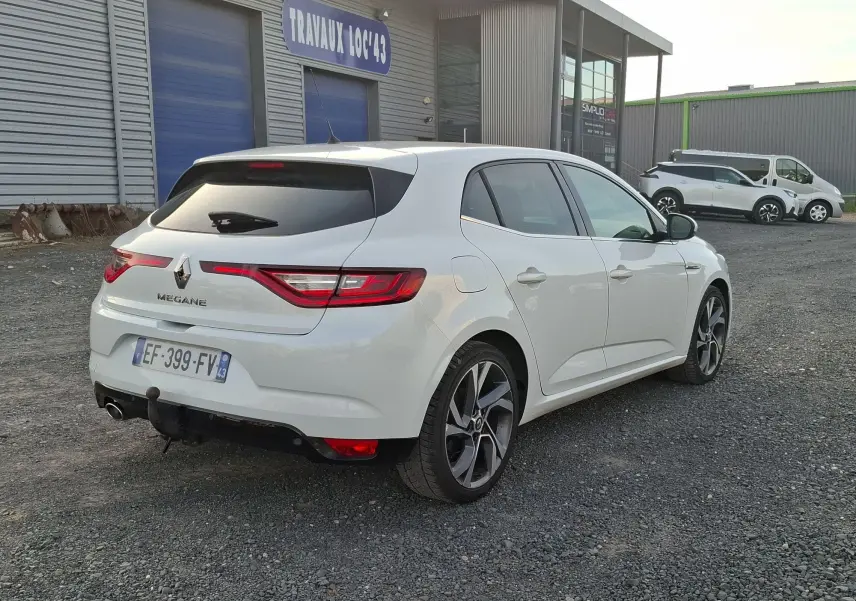Vue 3/4 arrière droite d'une Renault Mégane blanche 2016 avec attelage et jantes alliage noires et argentées.