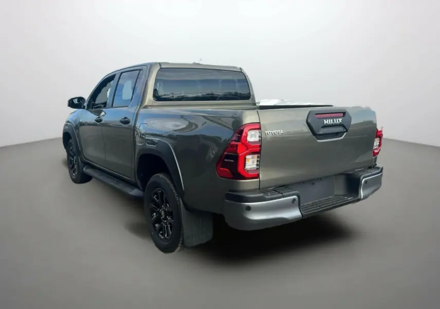 Toyota Hilux 4x4 2025 en bronze impérial, vue 3/4 arrière côté gauche avec benne et jantes noires.