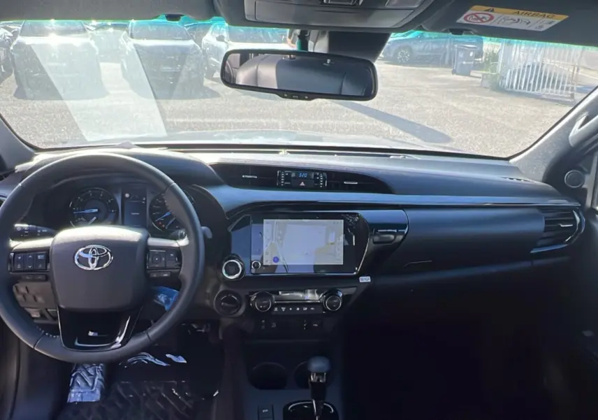 Vue intérieure frontale du Toyota Hilux 4x4 Invincible 2025, tableau de bord noir avec écran tactile central et volant multifonction.