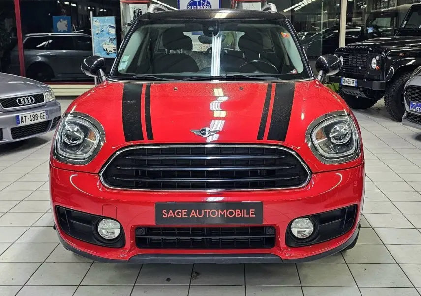 Vue avant d'une MINI Cooper Countryman rouge avec bandes noires sur le capot, en intérieur showroom.