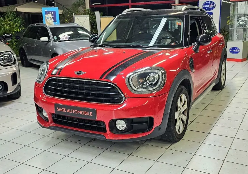 Vue 3/4 avant d'une MINI Cooper Countryman rouge avec bandes noires sur le capot, en showroom intérieur.
