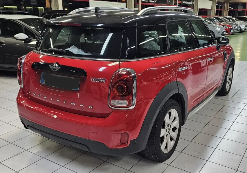 Vue 3/4 arrière droite d'une MINI Cooper Countryman rouge avec toit noir, dans un showroom intérieur.