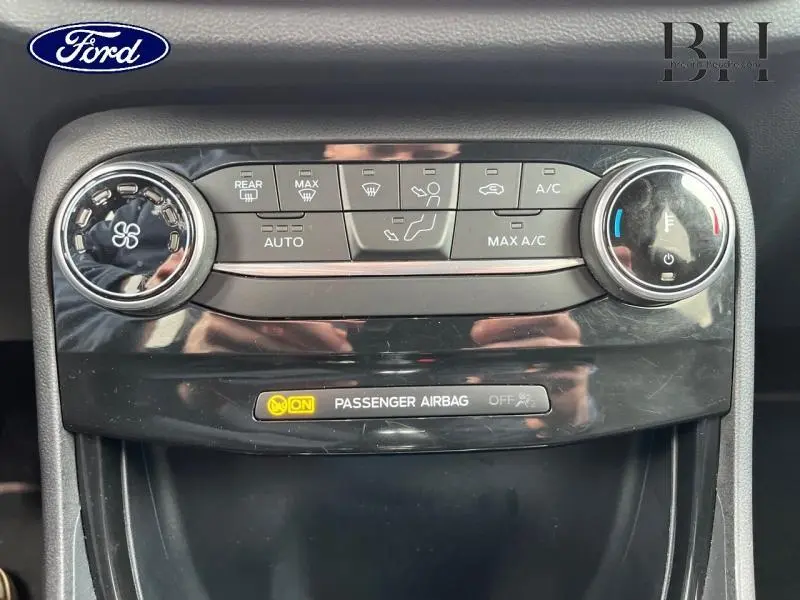 Vue rapprochée du panneau de commande de climatisation du Ford Puma noir, avec réglages de ventilation et indication airbag passager activé.