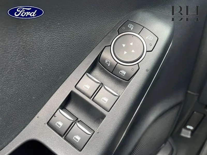 Gros plan sur les commandes de vitres électriques et rétroviseurs du côté conducteur d'un Ford Puma noir Agate Métallisée.