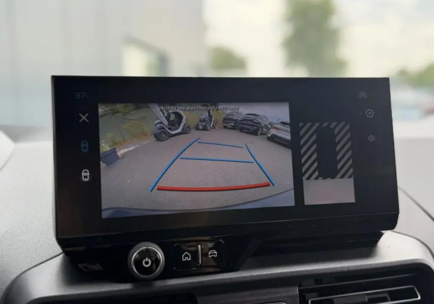 Écran tactile intérieur montrant la caméra de recul du Peugeot Rifter vert Sirkka en stationnement, vue arrière.