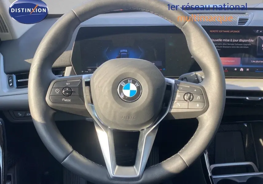 Volant en cuir noir avec logo BMW au centre, tableau de bord numérique et écran tactile du BMW X1 18I 2024 visible de face.