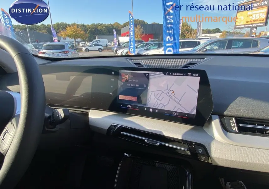 Vue intérieure du tableau de bord du BMW X1 18I 2024 avec écran tactile affichant la navigation et la radio.