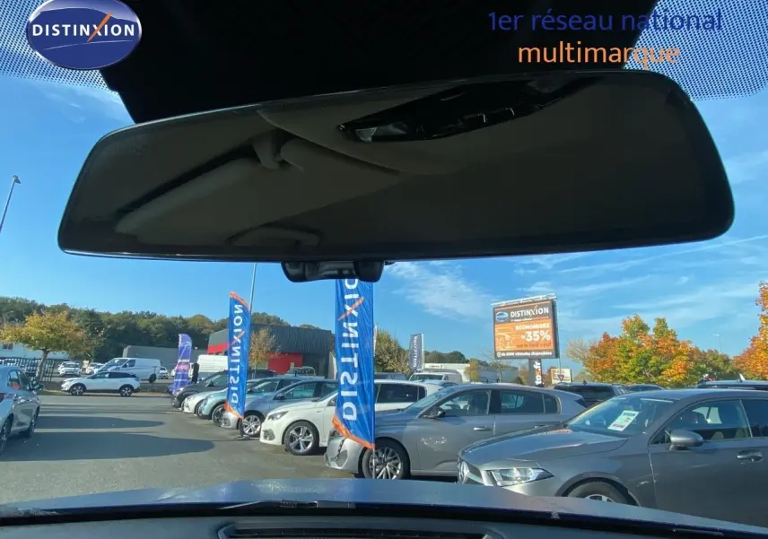 Vue depuis l'intérieur vers l'avant d'un BMW X1 bleu phytonic metal, avec plusieurs voitures en arrière-plan sur un parking.
