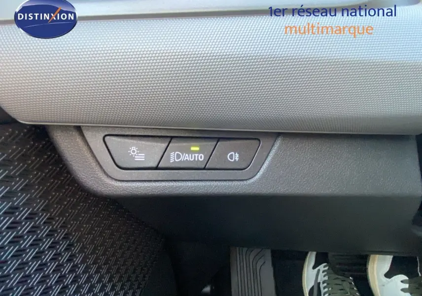 Panneau de commande des phares avec mode automatique allumé, situé sous le tableau de bord d'un BMW X1 bleu phytonic metal.