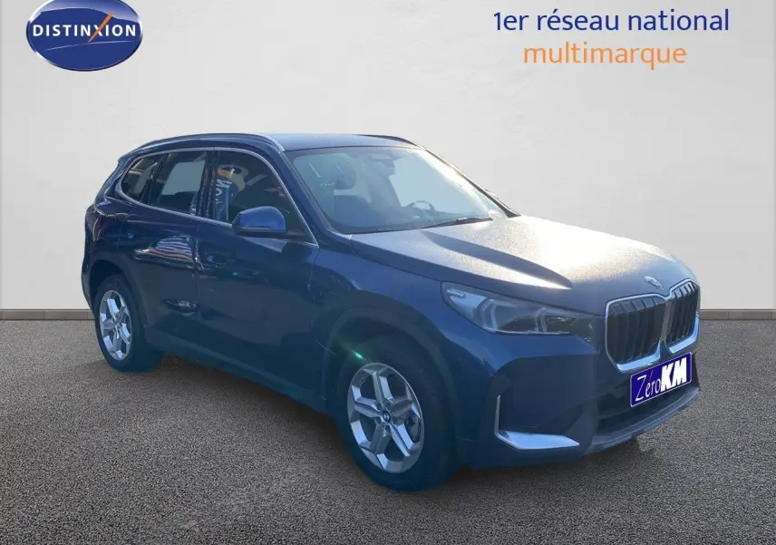BMW X1 18I bleu Phytonic Metal en 3/4 avant droit, avec calandre imposante et jantes argentées.