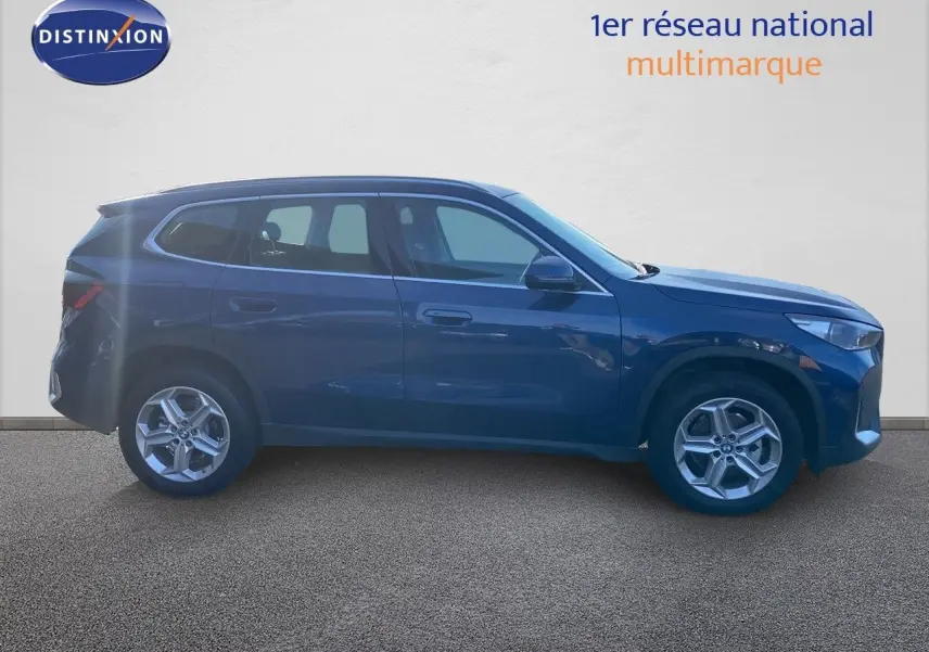 Profil côté gauche d'un BMW X1 18I 136CH Business Design bleu Phytonic Metal sur fond neutre.
