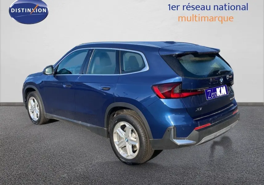 BMW X1 18I bleu Phytonic metal vu de l'arrière côté gauche, mettant en valeur ses feux LED et ses jantes argentées.