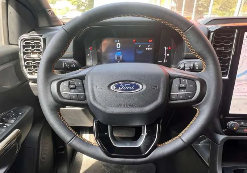 Vue rapprochée du volant en cuir avec surpiqûres marron du Ford Ranger 2025 Wildtrak Plus, tableau de bord numérique visible.