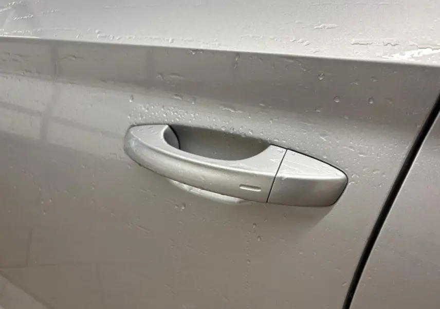 Poignée de porte côté gauche gris argent métallisé du Skoda Kamiq 2025 avec gouttes d'eau visibles.