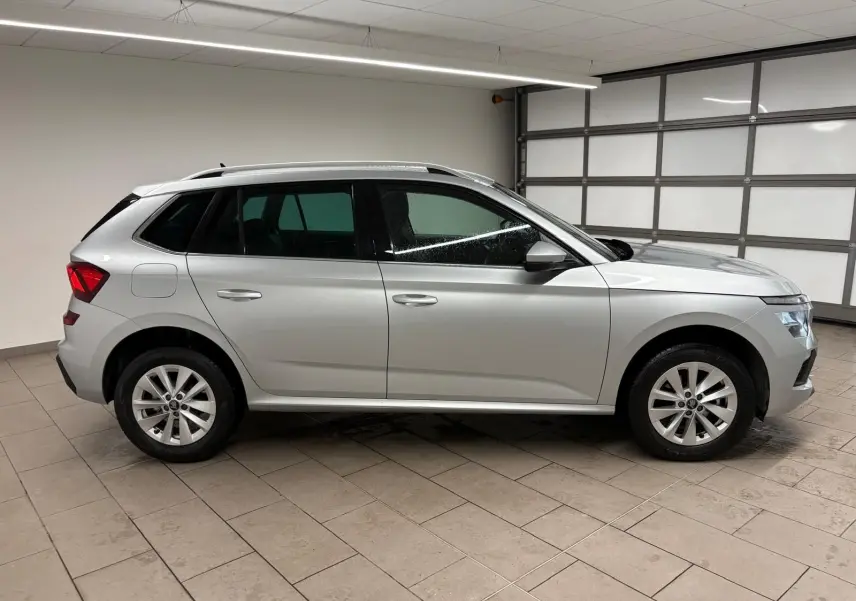 Vue de profil côté gauche d'un Skoda Kamiq gris argent métallisé dans un garage, avec caméra de recul visible.